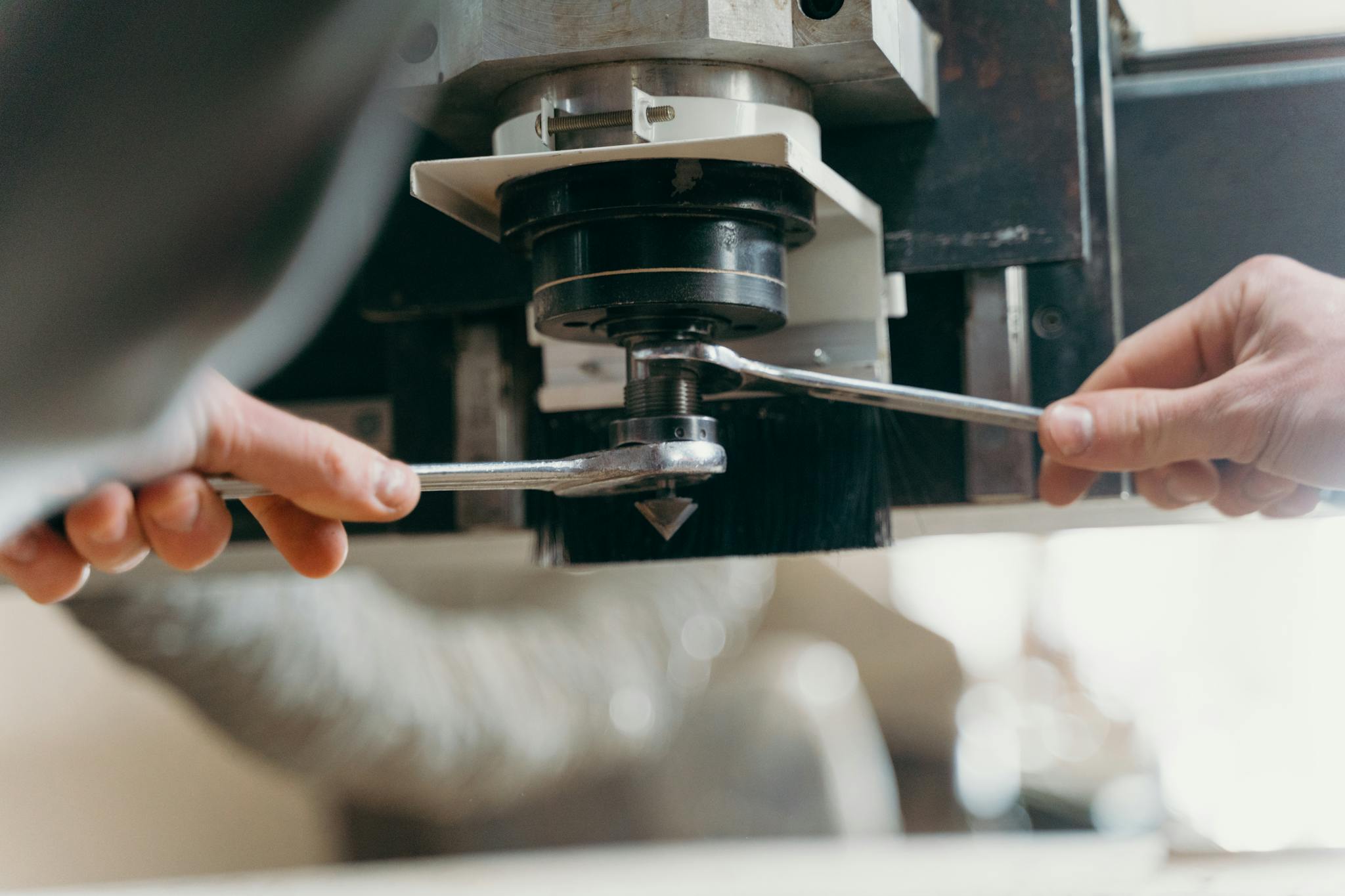 Close-up of hands adjusting a CNC machine using wrenches in an industrial setting.